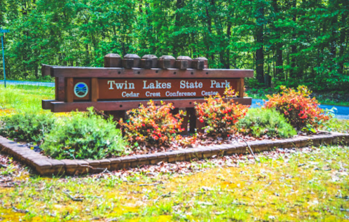 Sign for Twin Lakes State Park with colorful flowers and trees in the background, indicating the Cedar Crest Conference Center.