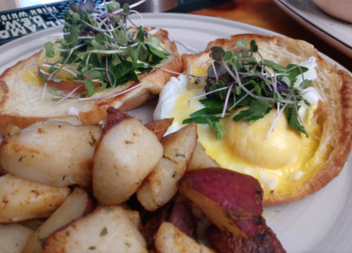 Two poached eggs on toasted bread topped with greens and microgreens, served with seasoned roasted potatoes.