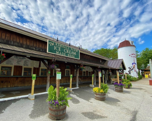 A rustic ice cream shop with a sign reading "Kimball Farm Ice Cream Made Here" and a white silo in the background.