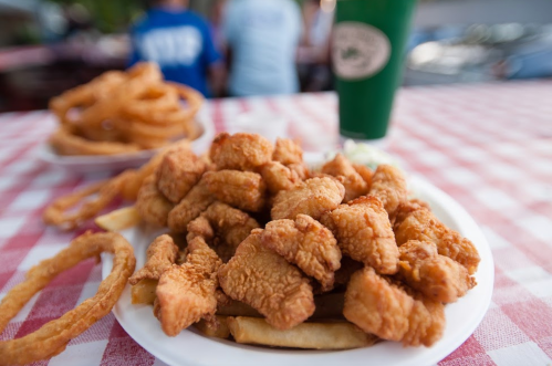 A plate of crispy fried chicken pieces served with fries and onion rings, set on a checkered tablecloth.