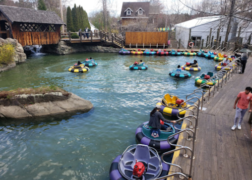 A view of a water attraction with colorful bumper boats on a lake, surrounded by trees and a wooden structure.