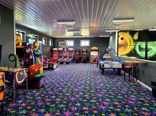 A colorful arcade room featuring various games, pinball machines, and vibrant star-patterned carpet.