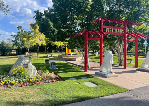 A peaceful park entrance with a red archway, stone lions, and colorful flowers under a blue sky.