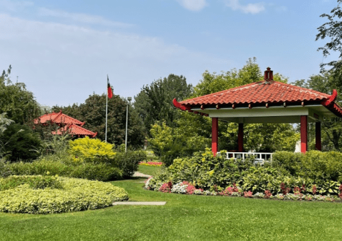 A serene garden featuring a red-roofed gazebo surrounded by lush greenery and colorful flower beds.