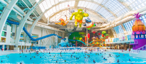 A vibrant indoor water park with a large pool, water slides, and colorful decorations, filled with people enjoying the water.