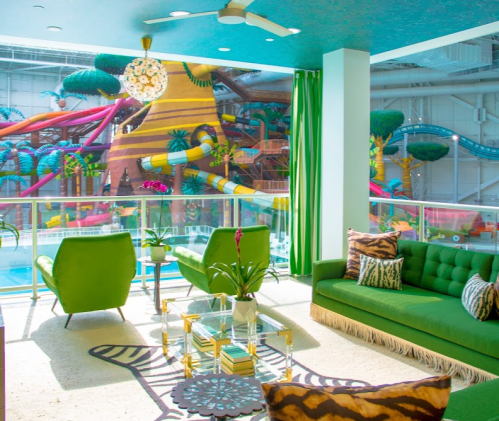 Brightly colored lounge area with green chairs and a sofa, overlooking a vibrant indoor water park.