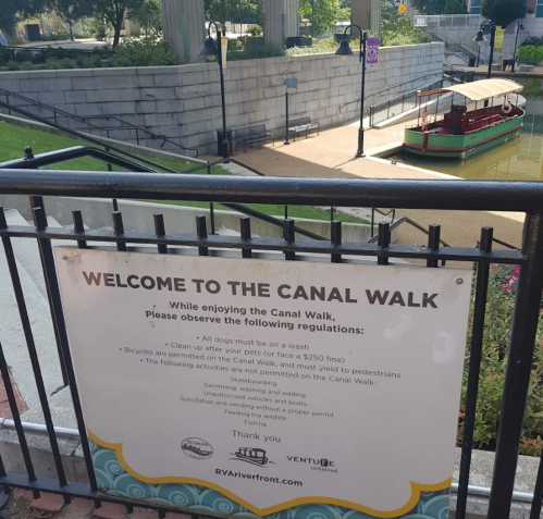 Sign at the Canal Walk outlining regulations for pets and pedestrians, with a boat docked nearby.