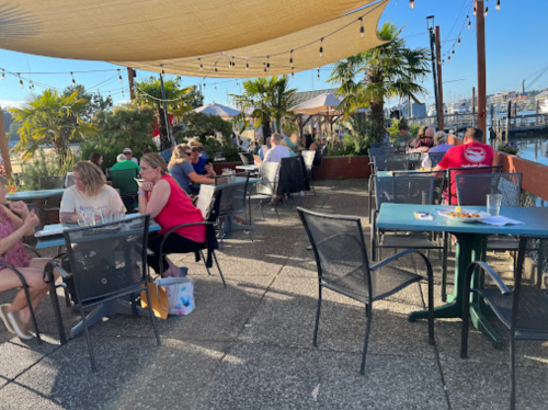 Outdoor dining area with tables, patrons enjoying meals, and palm trees under a sunny sky.