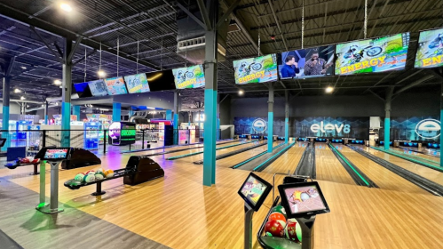 A vibrant bowling alley with multiple lanes, screens displaying games, and colorful lighting.