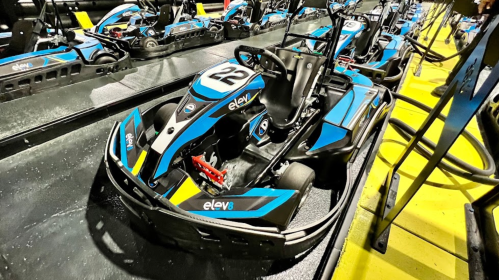 A blue and black go-kart with the number 22 parked on a track, surrounded by other karts in a racing facility.