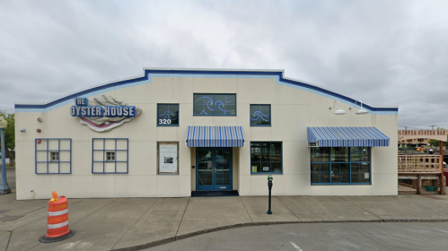 Exterior of The Oyster House, featuring blue and white striped awnings and a sign, with a construction cone in front.