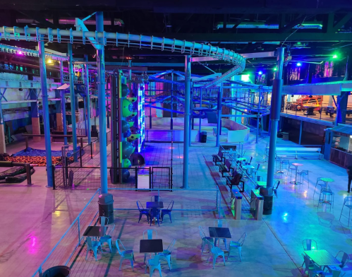 A brightly lit indoor amusement area featuring climbing structures, slides, and seating arrangements.