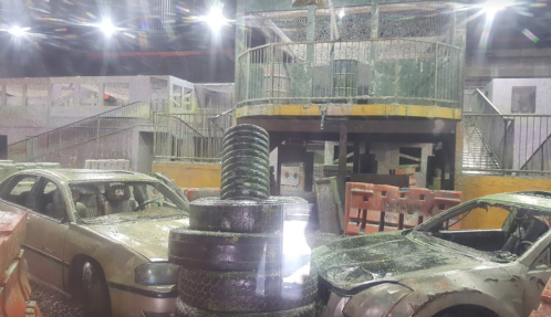 Abandoned cars and stacked tires in a dimly lit, industrial setting with debris and structures in the background.
