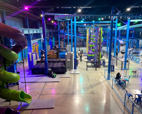 A vibrant indoor play area featuring slides, climbing structures, and people enjoying various activities.