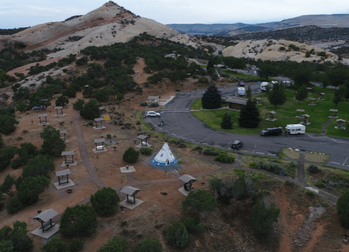 Aerial view of a campground with picnic areas, trees, and a road, set against a backdrop of rocky hills.