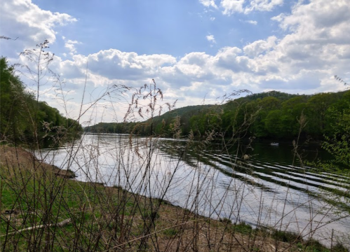 A serene river scene with gentle waves, surrounded by lush green hills and a partly cloudy sky.