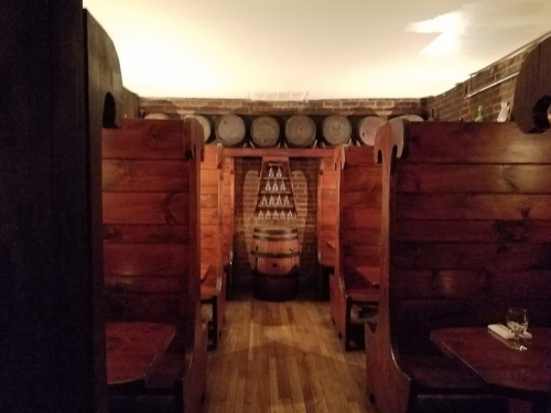 Cozy wooden booths in a rustic restaurant, with barrels and a stacked bottle display in the background.