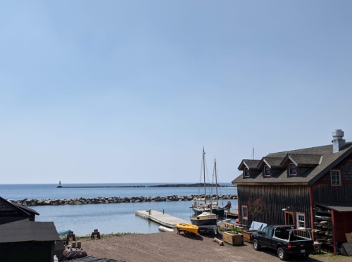 A serene waterfront scene featuring a dock, boats, and a rustic building against a clear blue sky.
