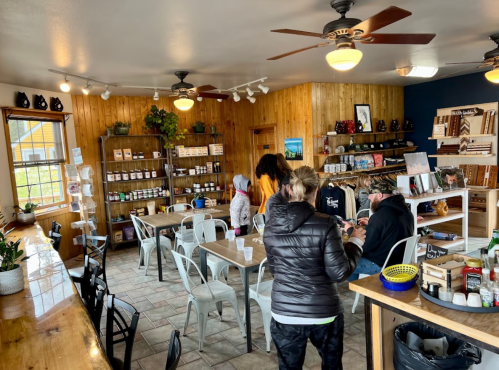 A cozy café interior with wooden walls, shelves of products, and customers chatting at tables.