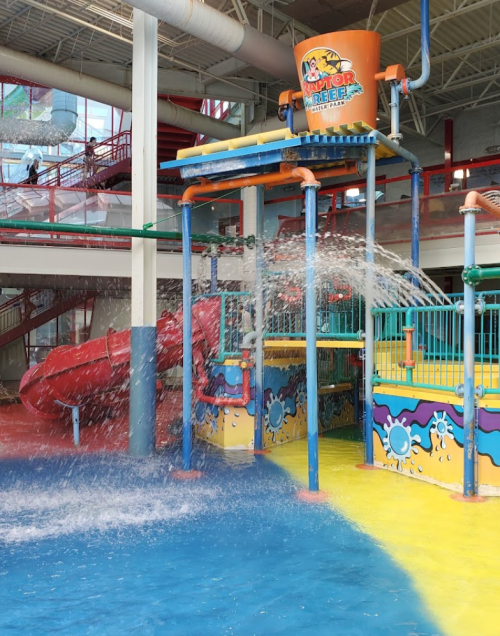 Colorful water play area with a large bucket tipping water, slides, and splashing features in a bright indoor setting.