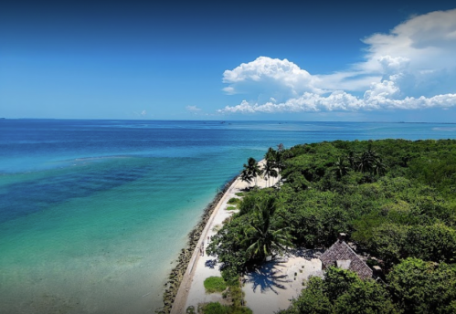 Aerial view of a tropical beach with clear blue water, lush greenery, and a small hut along the shoreline.