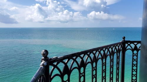 A view of the ocean from a balcony, featuring blue waters and a cloudy sky.