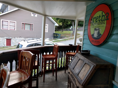 A porch with wooden chairs and a sign for Aretha Franklin's restaurant, overlooking a quiet street.
