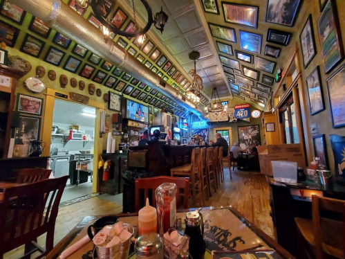 A cozy restaurant interior with framed photos on the walls, a bar area, and patrons enjoying their meals.