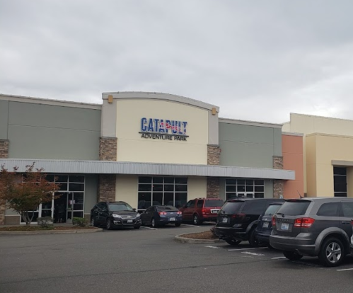 Exterior of Catapult Adventure Park building with parked cars in front and a cloudy sky.