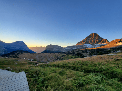 A scenic mountain landscape at sunset, featuring rugged peaks and a clear blue sky.