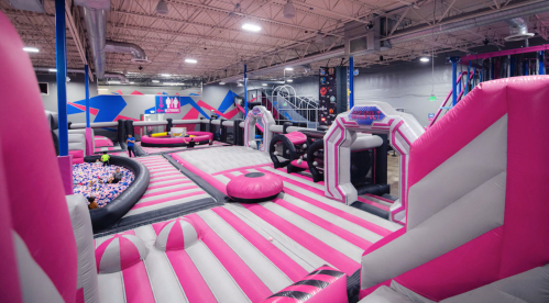 A vibrant indoor trampoline park featuring pink and black inflatable structures and a ball pit.