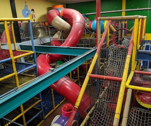 Colorful indoor play structure with slides, climbing nets, and tunnels in a vibrant children's play area.