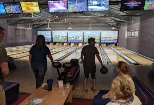 A bowling alley with several lanes, screens showing games, and people preparing to bowl.