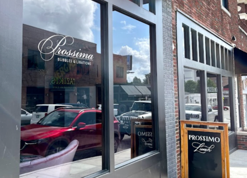 Exterior view of Prossima restaurant with large windows, showcasing the name and a lunch sign outside.