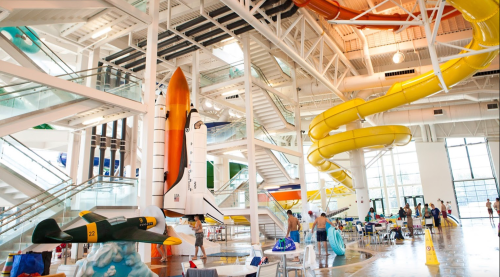 Indoor water park featuring a space shuttle, colorful water slides, and families enjoying the attractions.