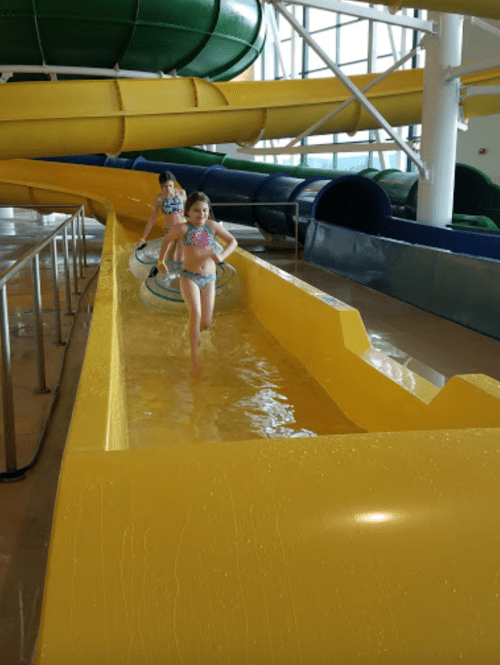 Two children in swimsuits play in a water slide area, splashing through shallow water and enjoying the fun.