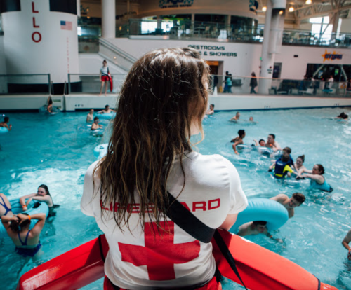 A lifeguard watches over a busy indoor pool filled with people enjoying the water.