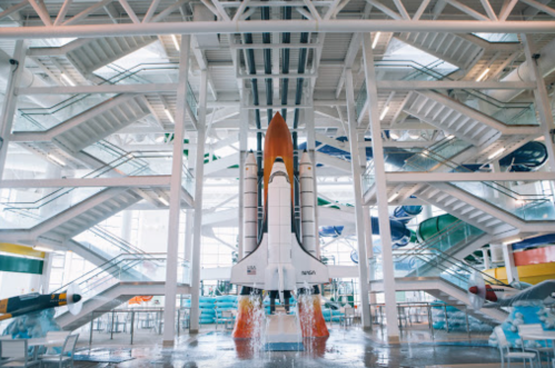 A large rocket model displayed in a modern building with multiple staircases and colorful murals.