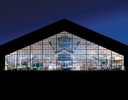 A large, modern building with a glass facade illuminated at night, showcasing its interior structure and design.