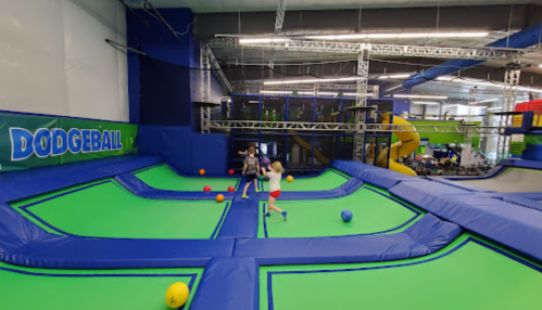 Two children playing dodgeball on a trampoline court with colorful balls and a vibrant, indoor play area.