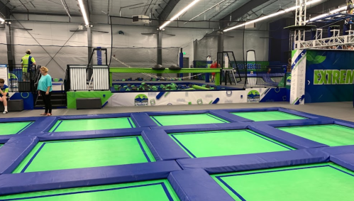 A spacious indoor trampoline park with green trampolines and various play areas, including climbing structures.