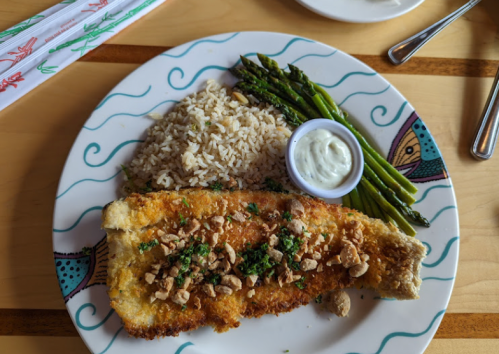 A plate with breaded fish, rice, asparagus, and a small cup of sauce, decorated with colorful patterns.