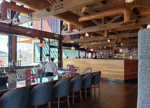 Interior of a modern restaurant featuring a bar, wooden accents, and large windows with a view.