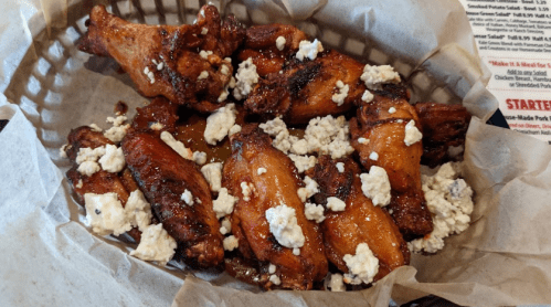 A basket of crispy chicken wings topped with crumbled blue cheese on a bed of parchment paper.