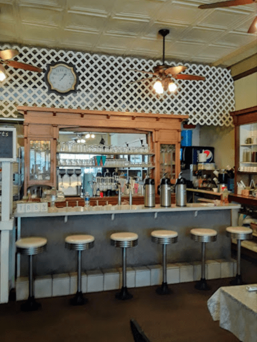 A vintage diner interior featuring a wooden counter, bar stools, and a decorative lattice wall.
