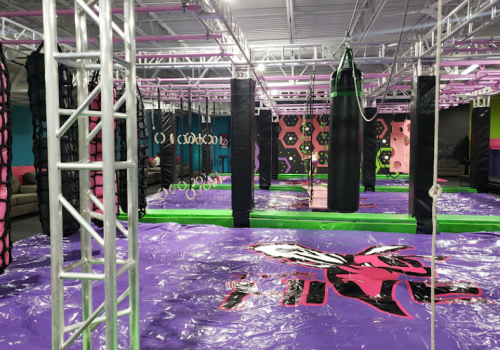 Indoor obstacle course featuring colorful mats, hanging rings, and climbing structures in a vibrant setting.