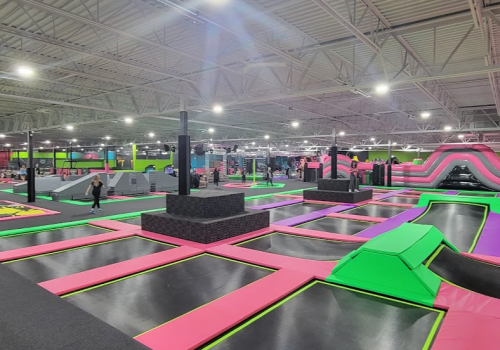 A vibrant indoor trampoline park with various jumping areas, ramps, and colorful padding. People are enjoying the space.