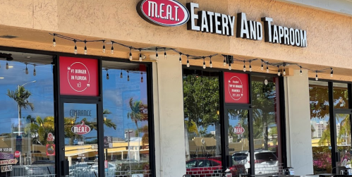 Exterior of M.E.A.T. Eatery and Taproom, featuring a sign and large windows with decorative lights.