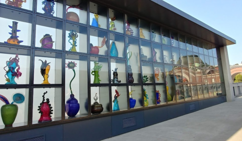 Colorful glass sculptures displayed in a large window, showcasing various shapes and designs against a clear sky.
