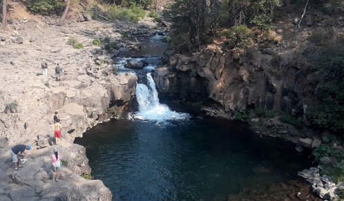 A scenic view of a waterfall surrounded by rocky terrain and people enjoying the natural landscape.